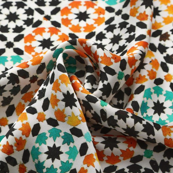 Detalle del Pañuelo Seda Nur plisado en espiral con motivos geométricos naranja y verde sobre blanco